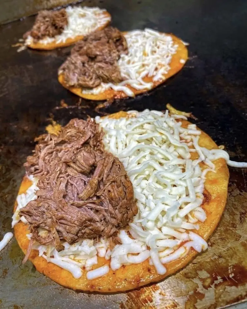 Shredded birria and cheese on tortillas on the grill