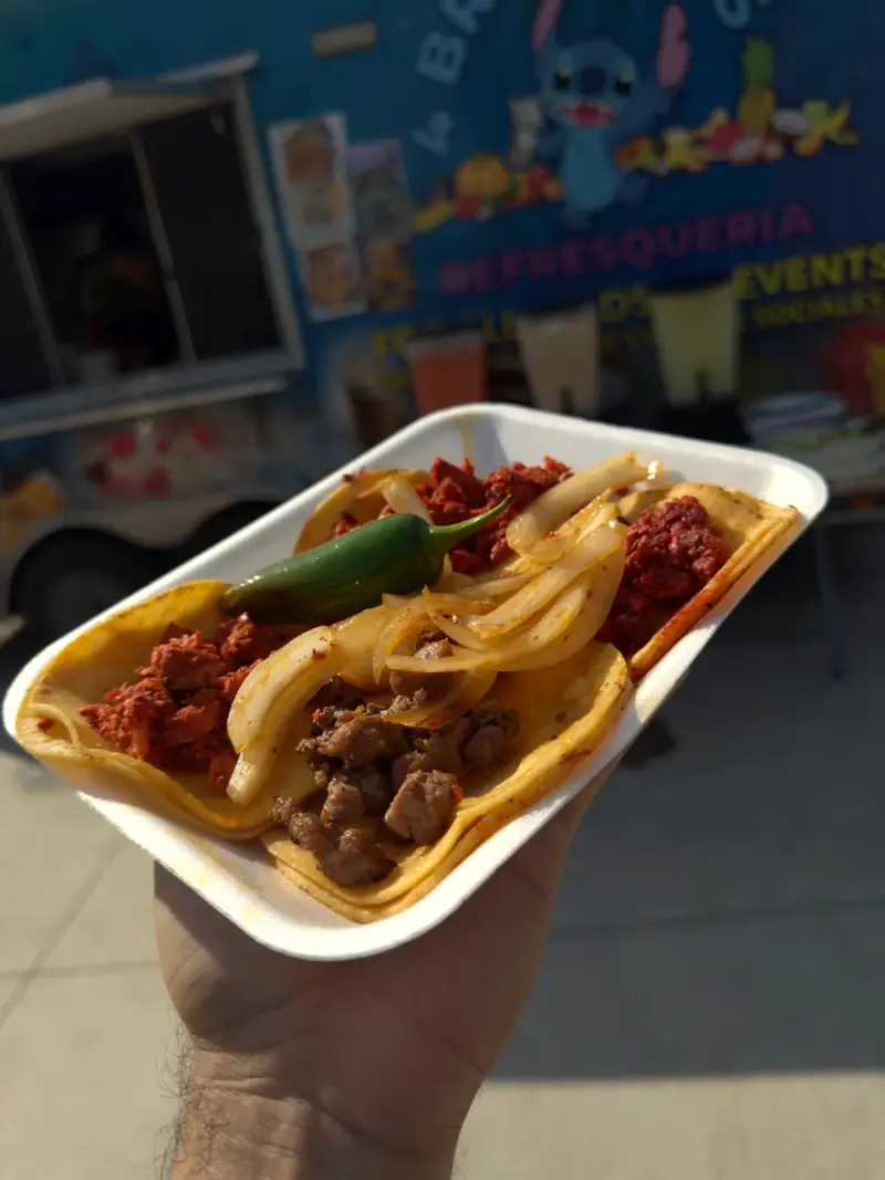 Tacos with grilled onions and a jalapeño held in front of the 4 Brothers truck