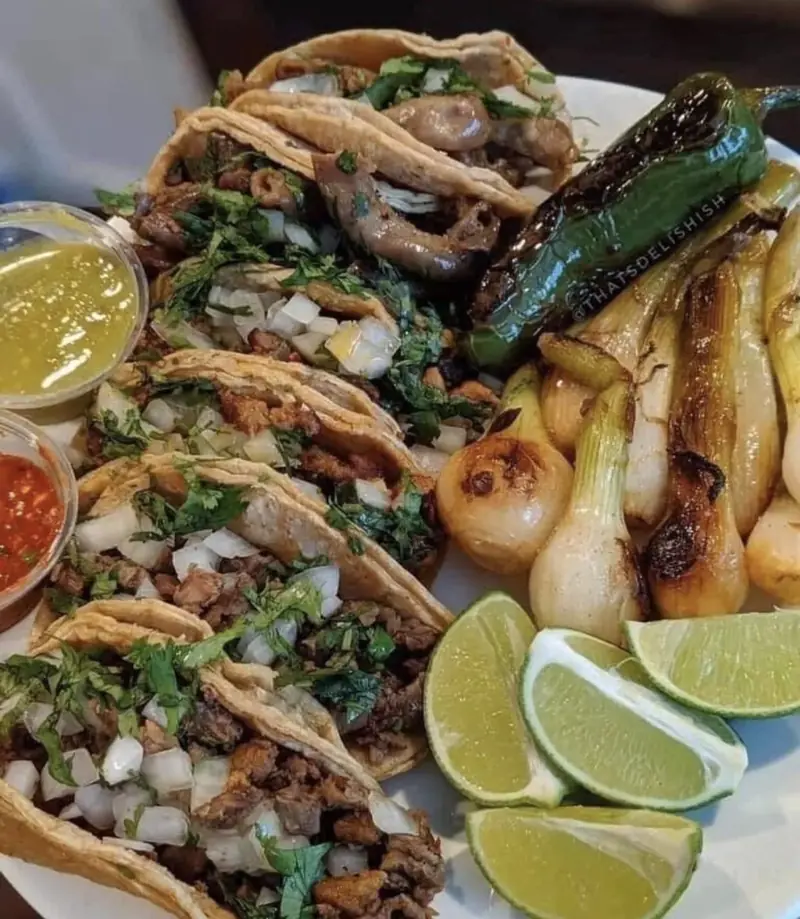 Plate of tacos with grilled onions, peppers and limes